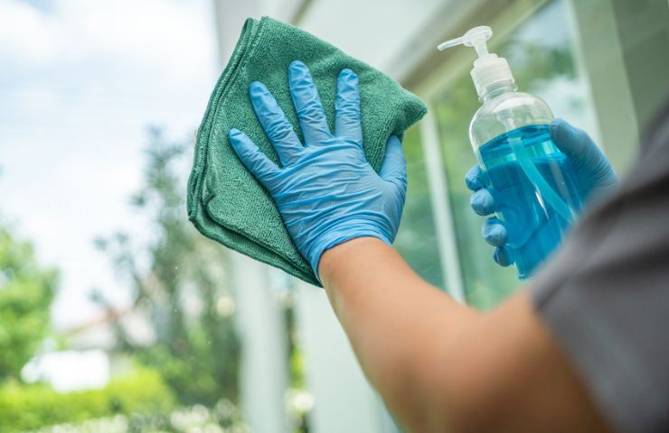 Persona che pulisce vetro e tieni in mano un panno verde e un detergente